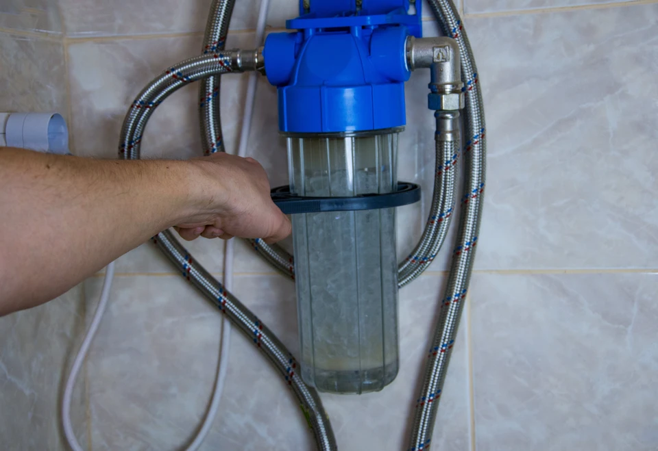 Intérieur carrelé blanc, main masculine manipulant un système de filtration d'eau