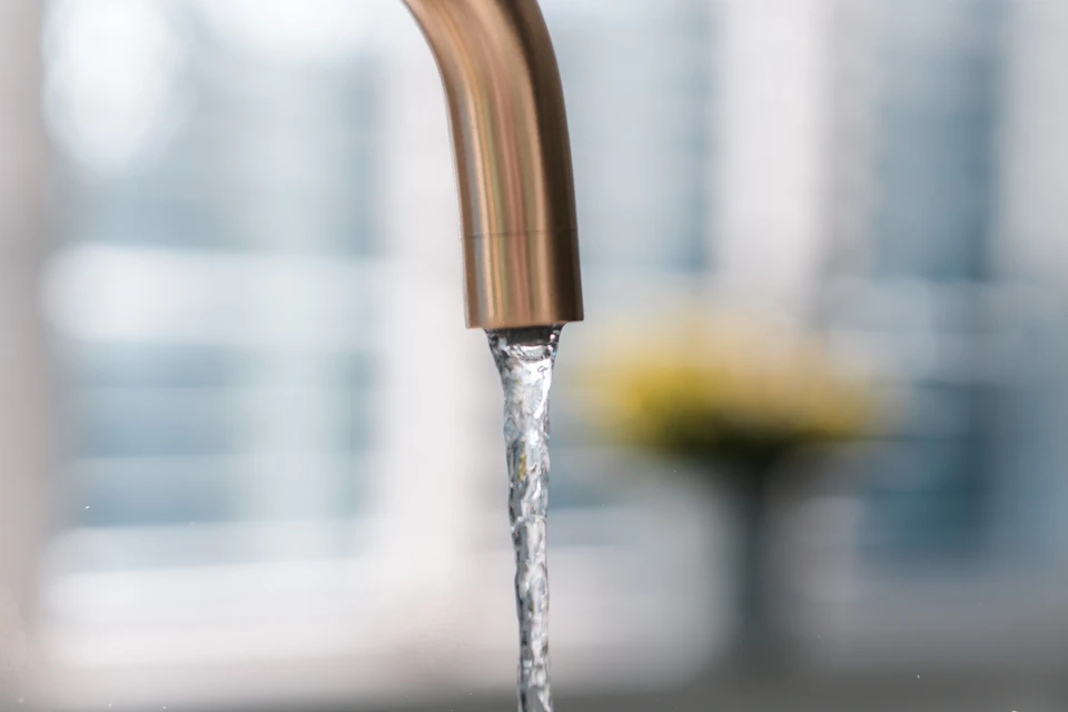 Photographie en gros plan d'un adoucisseur d'eau blanc ou gris légèrement oxydé ou présentant des signes d'usure visible (calcaire accumulé, taches, patine d'âge), installé sous un évier de cuisine domestique. L'image doit montrer l'équipement défaillant de manière claire et représentative de l'état problématique mentionné, dans un contexte résidentiel réaliste. Pas de personne, pas de texte visible.